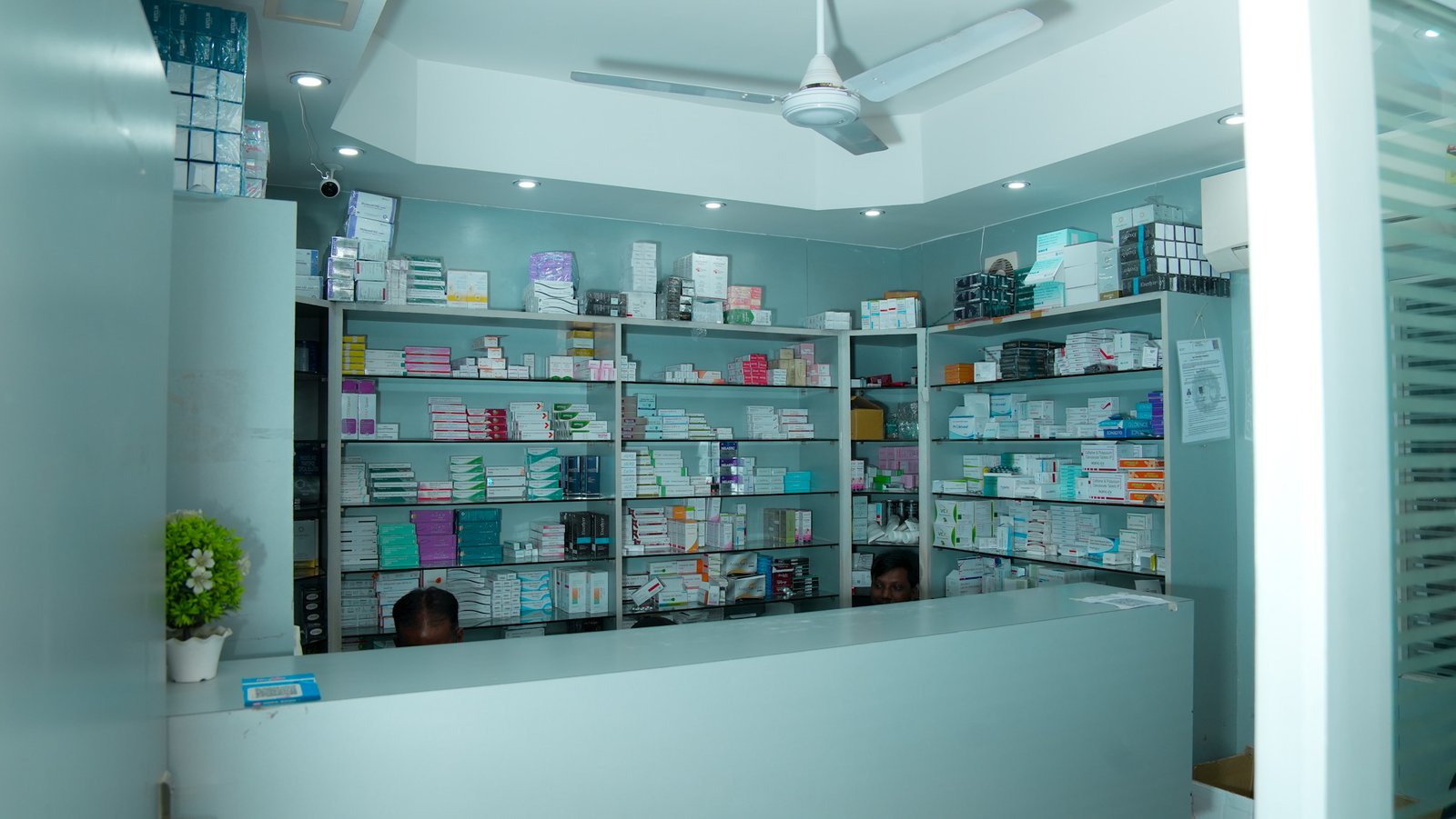 The pharmacy area of Dr. Hemnani’s Cosmoderm clinic shows shelves stocked with a wide range of medicines. Two staff members are partially visible behind the counter, ready to assist patients.